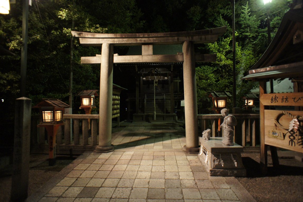 A torii gate and small shrine lit by stone lanterns at night